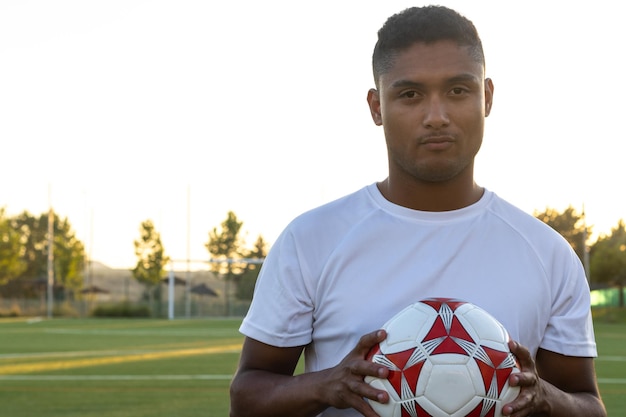 Ritratto di giocatore di calcio che tiene la palla all'aperto Giovane giocatore in possesso di un pallone da calcio sul campo da gioco