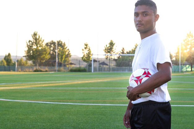 Ritratto di giocatore di calcio che tiene la palla all'aperto Giovane giocatore in possesso di un pallone da calcio sul campo da gioco