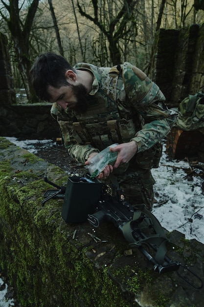 Ritratto di giocatore di softair in attrezzatura professionale carica una pistola con proiettili nella foresta. Soldato con armi in guerra