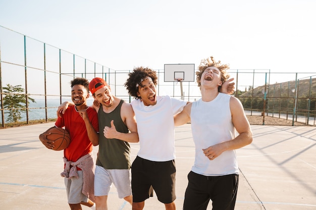 Ritratto di giocatori di basket uomini sportivi felici camminando lungo il parco giochi all'aperto, durante la giornata di sole estivo