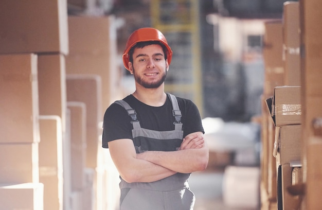 Ritratto di giovane addetto allo stoccaggio in magazzino in uniforme e elmetto.