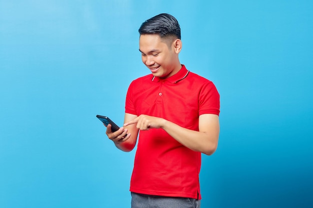 Ritratto di giovane asiatico bello allegro che utilizza e invia messaggi di testo con lo smartphone su sfondo blu