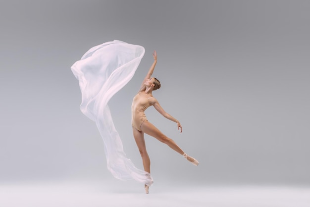 Ritratto di giovane ballerina che balla con tessuto bianco trasparente isolato sopra studio grigio