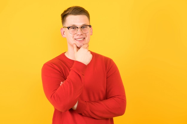 Ritratto di giovane bel ragazzo sorridente in maglione rosso che tiene la sua mano vicino al pensiero del mento