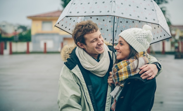 Ritratto di giovane bella coppia che abbraccia e ride sotto l'ombrellone in una giornata di pioggia autunnale. Amore e concetto di relazioni di coppia.