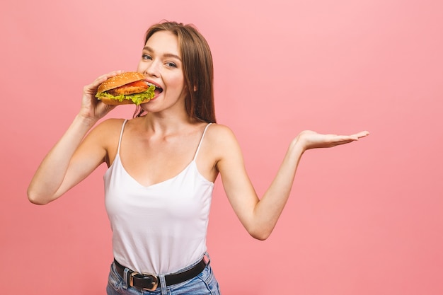 Ritratto di giovane bella donna affamata che mangia hamburger