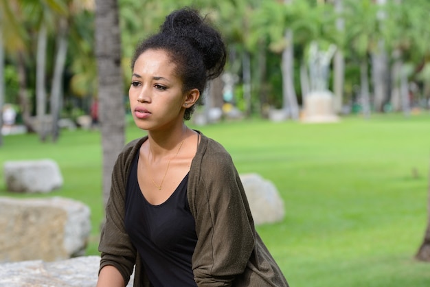 Ritratto di giovane bella donna africana con capelli afro che si distende al parco all'aperto