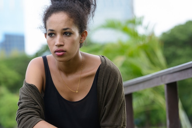 Ritratto di giovane bella donna africana con capelli afro che si distende al parco all'aperto