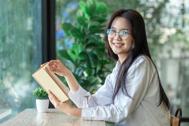 Ritratto di giovane bella donna asiatica che legge un libro mentre si rilassa durante il lavoro a casa