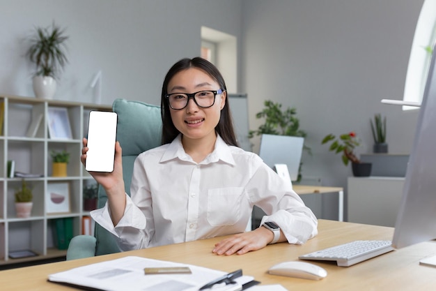 Ritratto di giovane bella donna asiatica con gli occhiali che tiene un telefono cellulare in mano che mostra il