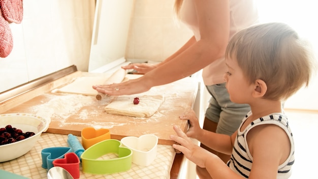 Ritratto di giovane bella donna che insegna al suo bambino a preparare biscotti e cuocere torte in cucina a casa