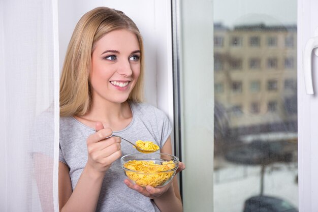 Ritratto di giovane bella donna che mangia i fiocchi di mais a casa