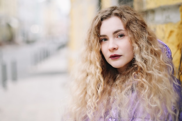 Ritratto di giovane bella donna con capelli ricci blondie all'aperto. Bellezza, concetto di moda. Stile di strada. Sfondo bokeh