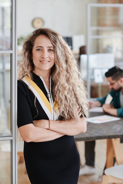 Ritratto di giovane bella donna d'affari che sorride alla macchina fotografica mentre lavora in ufficio con i suoi colleghi