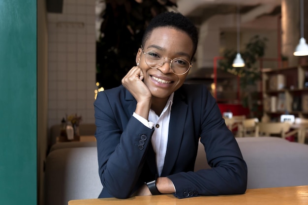 Ritratto di giovane bella donna d'affari, sorridente e gioiosa, seduta nel bar del ristorante, donna afroamericana che ha pausa pranzo