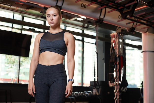 Ritratto di giovane bella donna in abbigliamento sportivo che guarda l'obbiettivo mentre levandosi in piedi in palestra