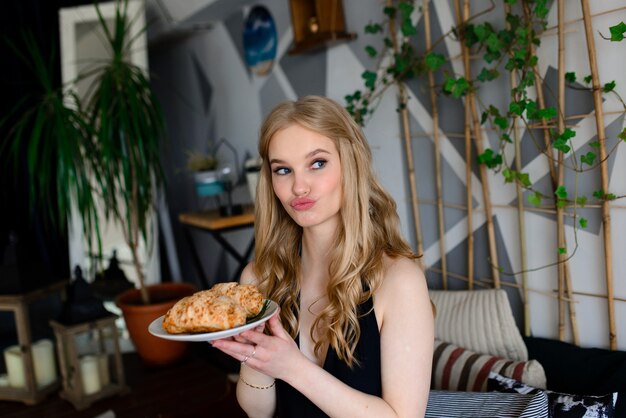 Ritratto di giovane bella donna in biancheria, costume da bagno nero con una torta dolce, croissant