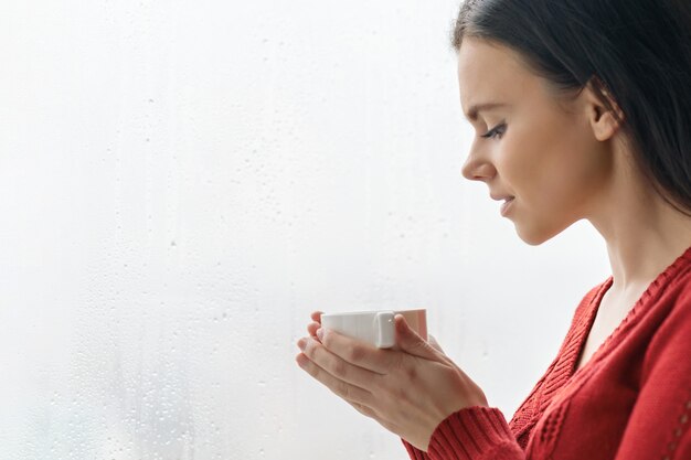 Ritratto di giovane bella donna in maglione rosso che beve caffè.