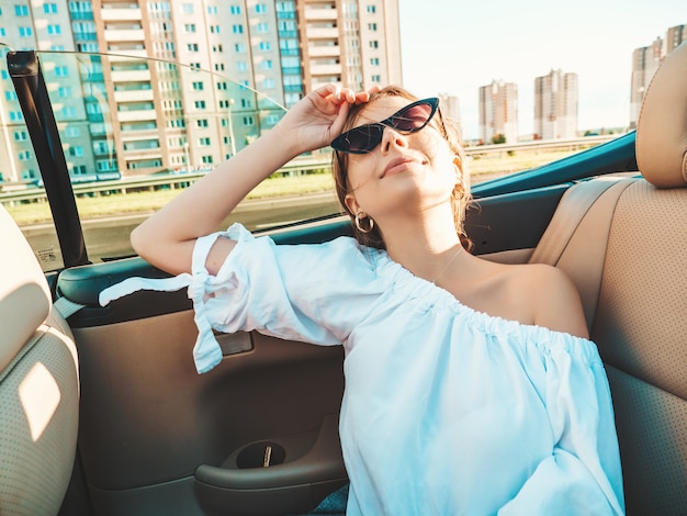 Ritratto di giovane bella e sorridente ragazza hipster in auto decappottabile