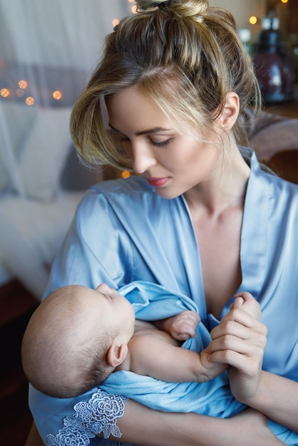 Ritratto di giovane bella madre con il suo piccolo bambino sveglio avvolto nel panno blu