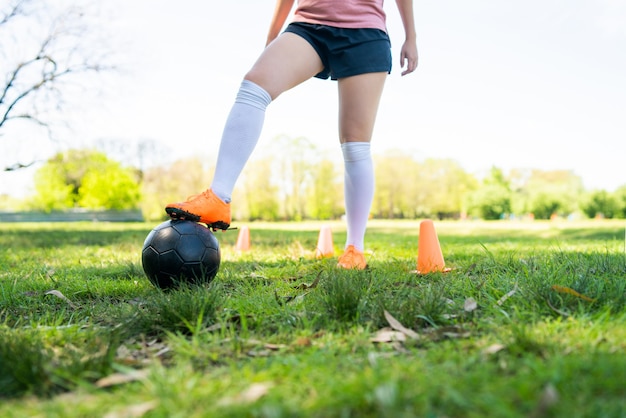 Ritratto di giovane calciatore femminile che corre intorno ai coni mentre si esercita con la palla sul campo. Concetto di sport.