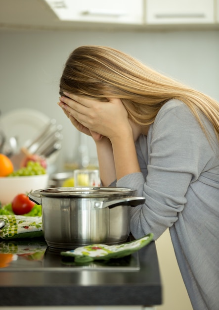 Ritratto di giovane casalinga esausta che posa sulla cucina mentre cucina la zuppa