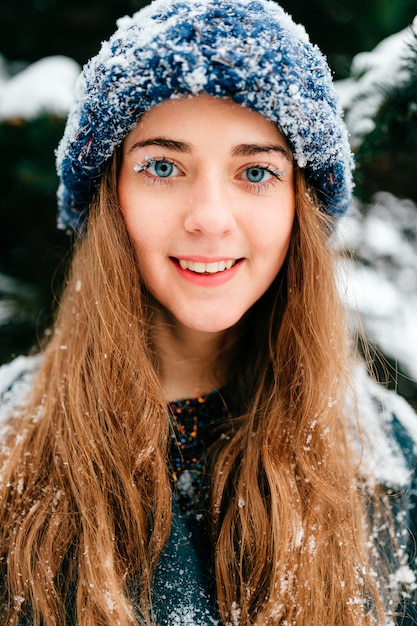 Ritratto di giovane castana abbastanza sorridente con neve che copre il suo fronte nel parco di inverno