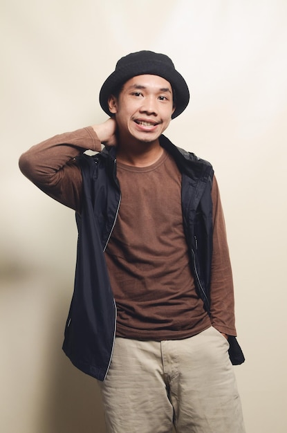 Ritratto di giovane college asiatico con gesto di saluto che indossa una maglietta marrone e un giubbotto nero