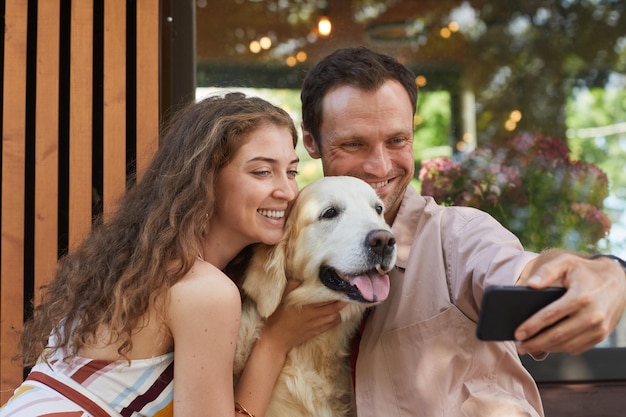 Ritratto di giovane coppia che prende selfie con il cane all'aperto nello spazio della copia di estate