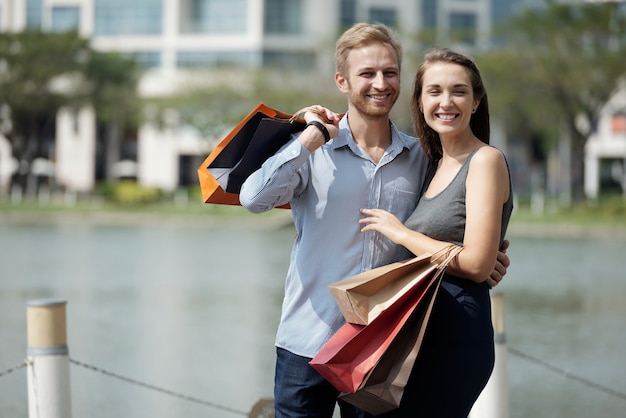 Ritratto di giovane coppia felice innamorata che tiene le borse della spesa in piedi all'aperto e sorri...