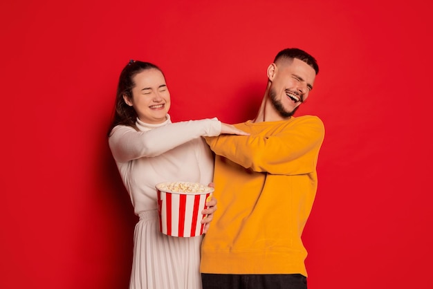 Ritratto di giovane coppia felice uomo e donna in posa con popcorn isolato su sfondo rosso