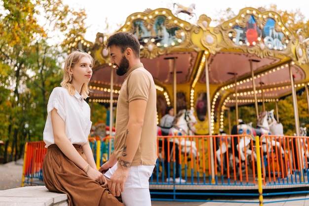 Ritratto di giovane coppia romantica innamorata seduta in piedi tenendosi per mano nel parco divertimenti sullo sfondo della giostra il giorno d'estate