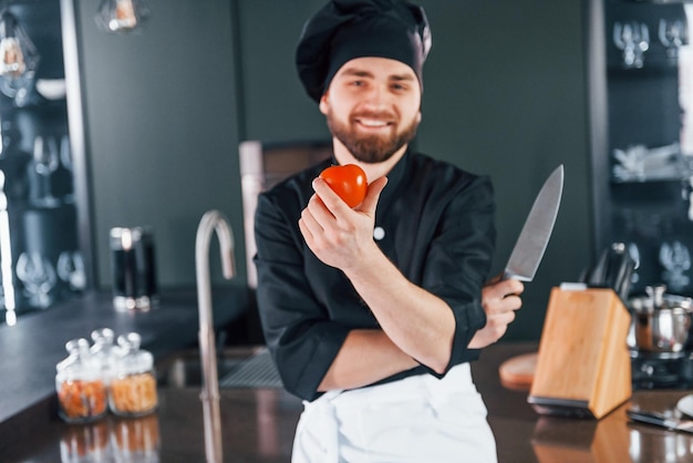 Ritratto di giovane cuoco professionista in uniforme che posa per la macchina fotografica in cucina