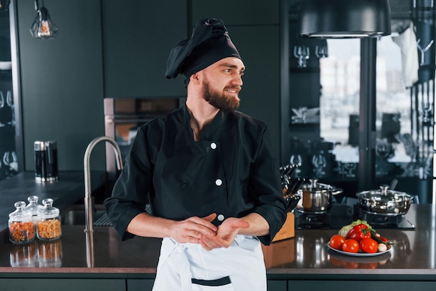 Ritratto di giovane cuoco professionista in uniforme che posa per la macchina fotografica in cucina