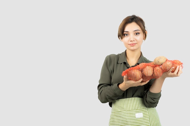 Ritratto di giovane donna adorabile dell'agricoltore che tiene le patate in borsa. Foto di alta qualità