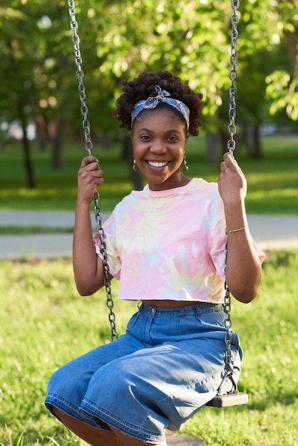 Ritratto di giovane donna africana che sorride alla macchina fotografica mentre è seduta su un'altalena nel parco
