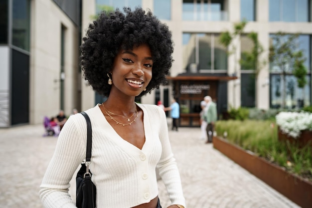 Ritratto di giovane donna africana con acconciatura afro sorridente in background urbano