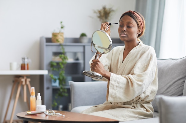 Ritratto di giovane donna afro-americana che fa il trucco a casa al mattino, copia spazio