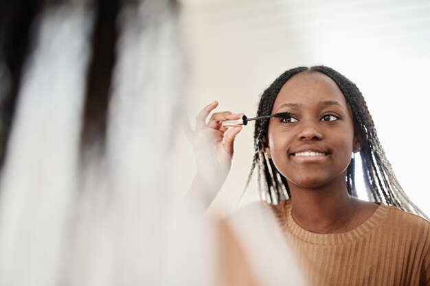 Ritratto di giovane donna afroamericana che si mette il mascara mentre si trucca la mattina e guarda...