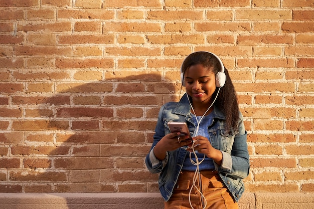 Ritratto di giovane donna afroamericana con le cuffie che ascolta la musica mentre si utilizza il suo telefono cellulare