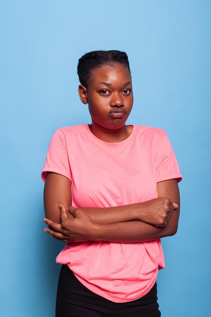 Ritratto di giovane donna afroamericana delusa arrabbiata che fa espressione furiosa in piedi in studio con sfondo blu. Studente infelice stressante che ha conflitto dell'adolescente. Concetto di dramma