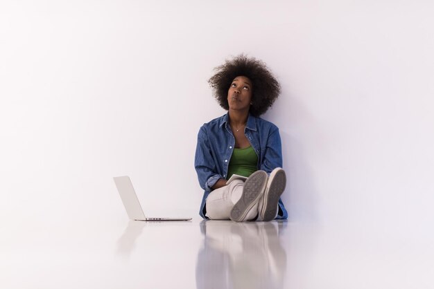 Ritratto di giovane donna afroamericana felice che si siede sul pavimento con il computer portatile
