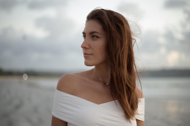 Ritratto di giovane donna al lato dell'oceano guardando la fotocamera Femmina sorridente in piedi sulla spiaggia