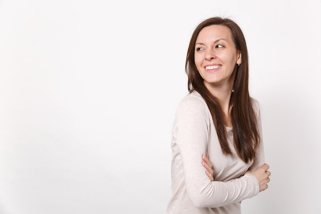 Ritratto di giovane donna allegra gioiosa in abiti leggeri che guarda da parte tenendo le mani piegate isolato su sfondo bianco muro in studio. Persone sincere emozioni, concetto di stile di vita. Mock up spazio di copia.