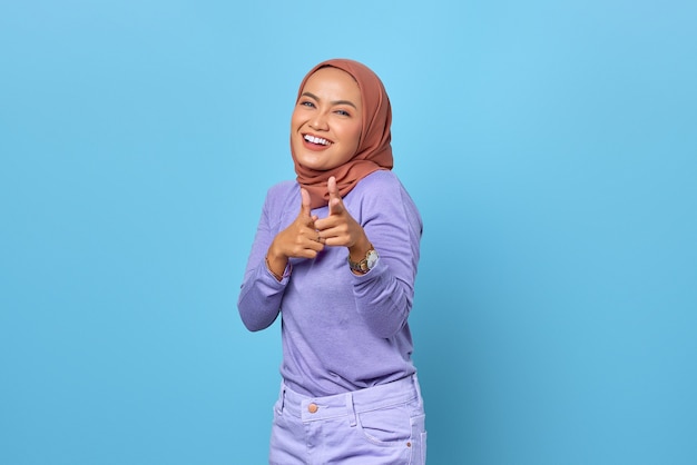 Ritratto di giovane donna asiatica allegra che punta il dito alla telecamera su sfondo blu