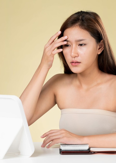 Ritratto di giovane donna asiatica ardente che si guarda allo specchio preoccuparsi del brufolo sul viso Cure di bellezza per il concetto di trattamento dell'acne con problemi di pelle