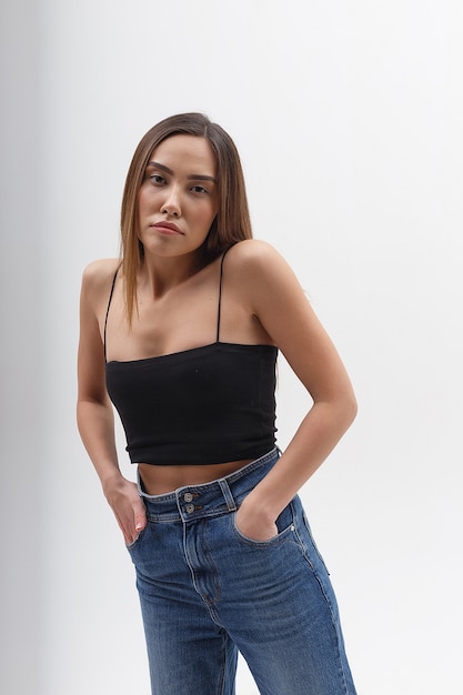 Ritratto di giovane donna asiatica attraente con capelli lunghi in top nero, blue jeans isolato su sfondo bianco studio. femmina graziosa magra in posa sul ciclorama. prove modello di bella signora