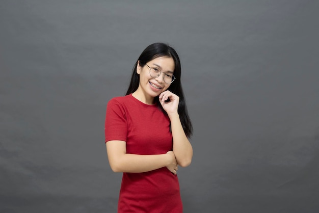 Ritratto di giovane donna asiatica bruna in un vestito rosso incrocia le braccia sul petto e determinato posato sorridente con fiducia girato in studio isolato su sfondo grigio