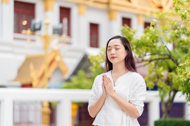 Ritratto di giovane donna asiatica che indossa abiti tradizionali della Thailandia pregando al Wat Ratchanatdaram