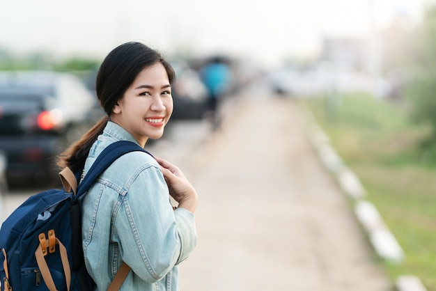 Ritratto di giovane donna asiatica che indossa giacca blu denim e zaino sorridente guardando indietro